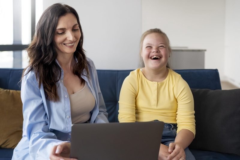 A mother and daughter laughing together while looking at a laptop at home