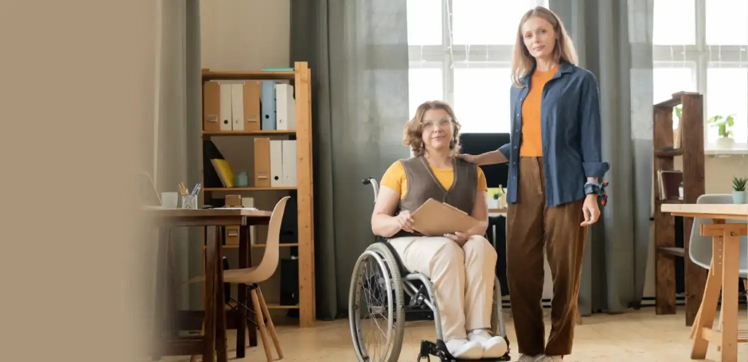 A colleague supporting a co-worker who uses a wheelchair in a bright, inclusive office